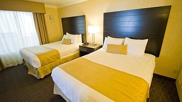 A hotel room with two beds, a nightstand with a lamp, and a window with curtains.