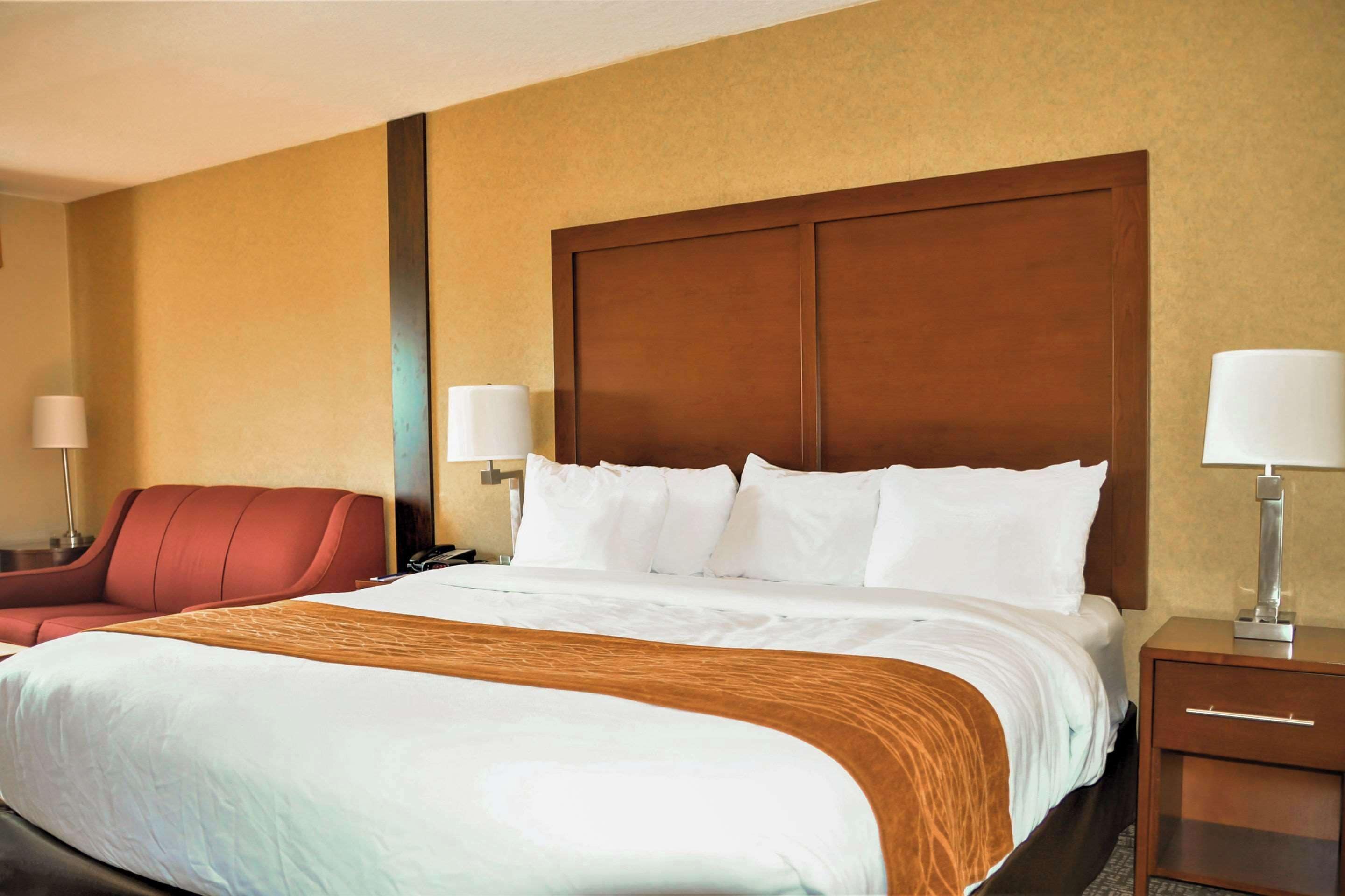A hotel room with a large bed, a wooden headboard, a red armchair, and two bedside lamps.