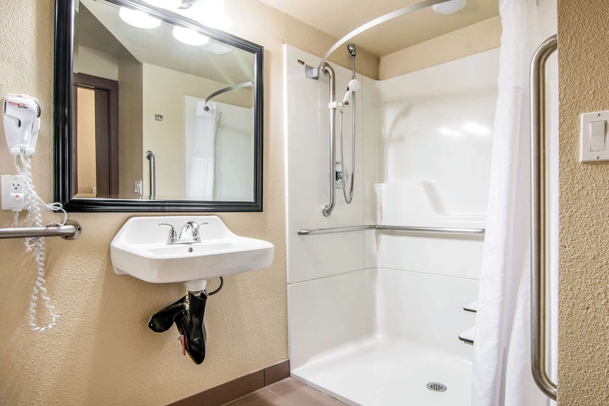 A bathroom with a white sink, a mirror, a hairdryer, and a walk-in shower.
