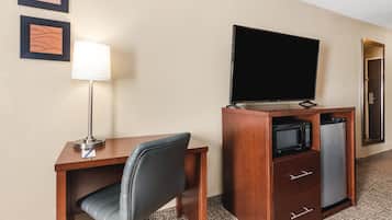 Une chambre d’hôtel équipée d’un bureau en bois, d’un fauteuil de bureau noir, d’un téléviseur à écran plat, d’un four à micro-ondes et d’un réfrigérateur.