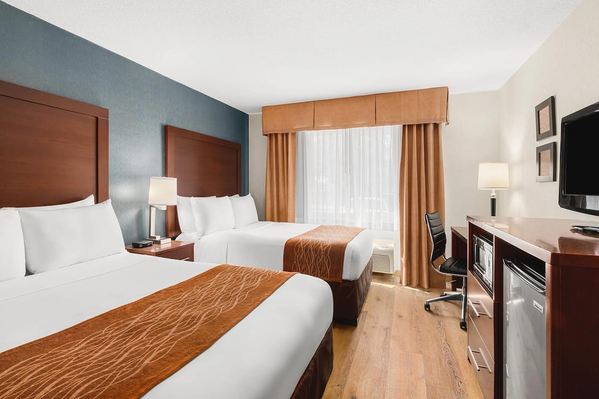 A hotel room with two beds, a desk, a television, and a window with curtains.