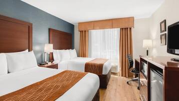 A hotel room with two beds, a desk, a television, and a window with curtains.