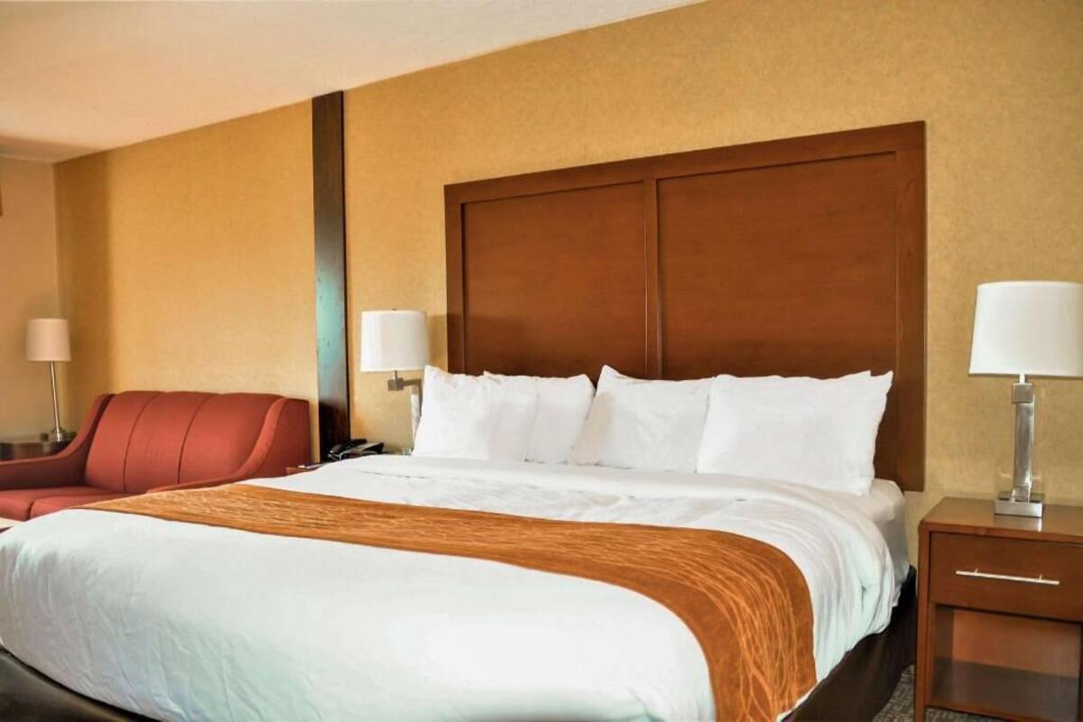 A hotel room with a large bed, a red chair, two bedside tables with lamps, and a wooden headboard.