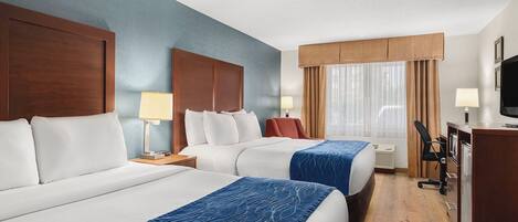 A hotel room with two beds, a desk, a chair, a television, and a window with curtains.