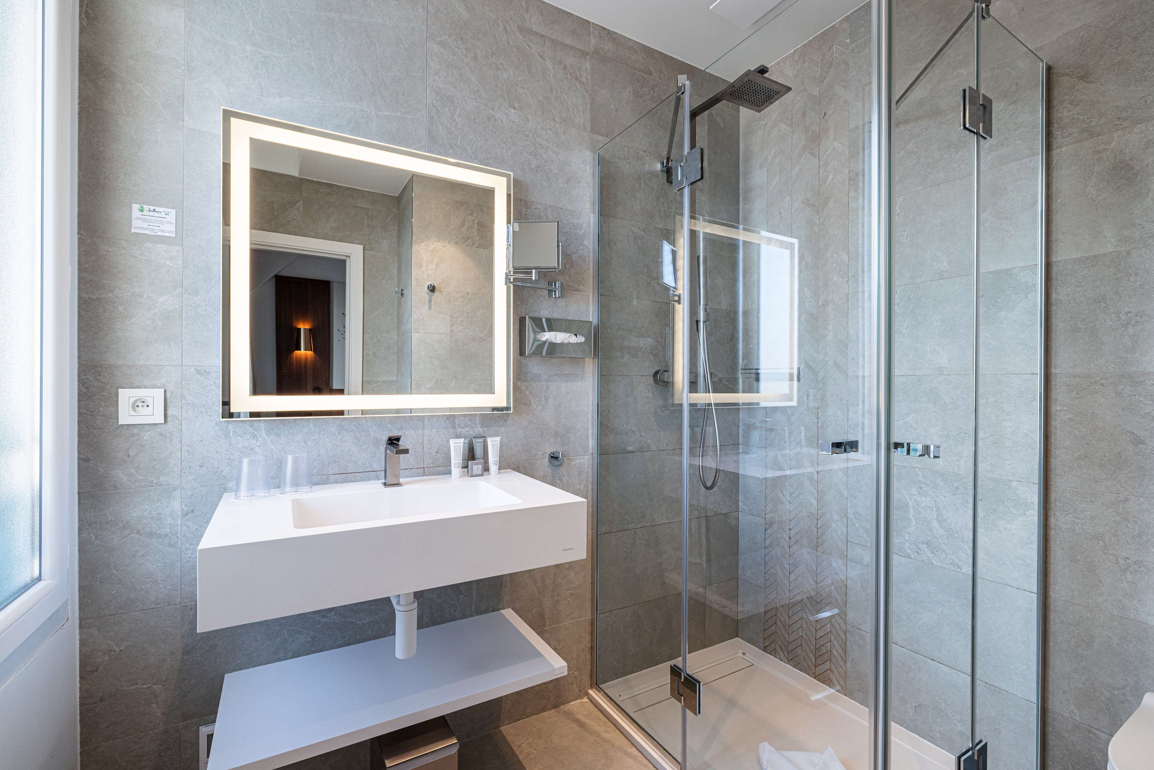 A modern bathroom with a large mirror, white sink, and glass shower enclosure.