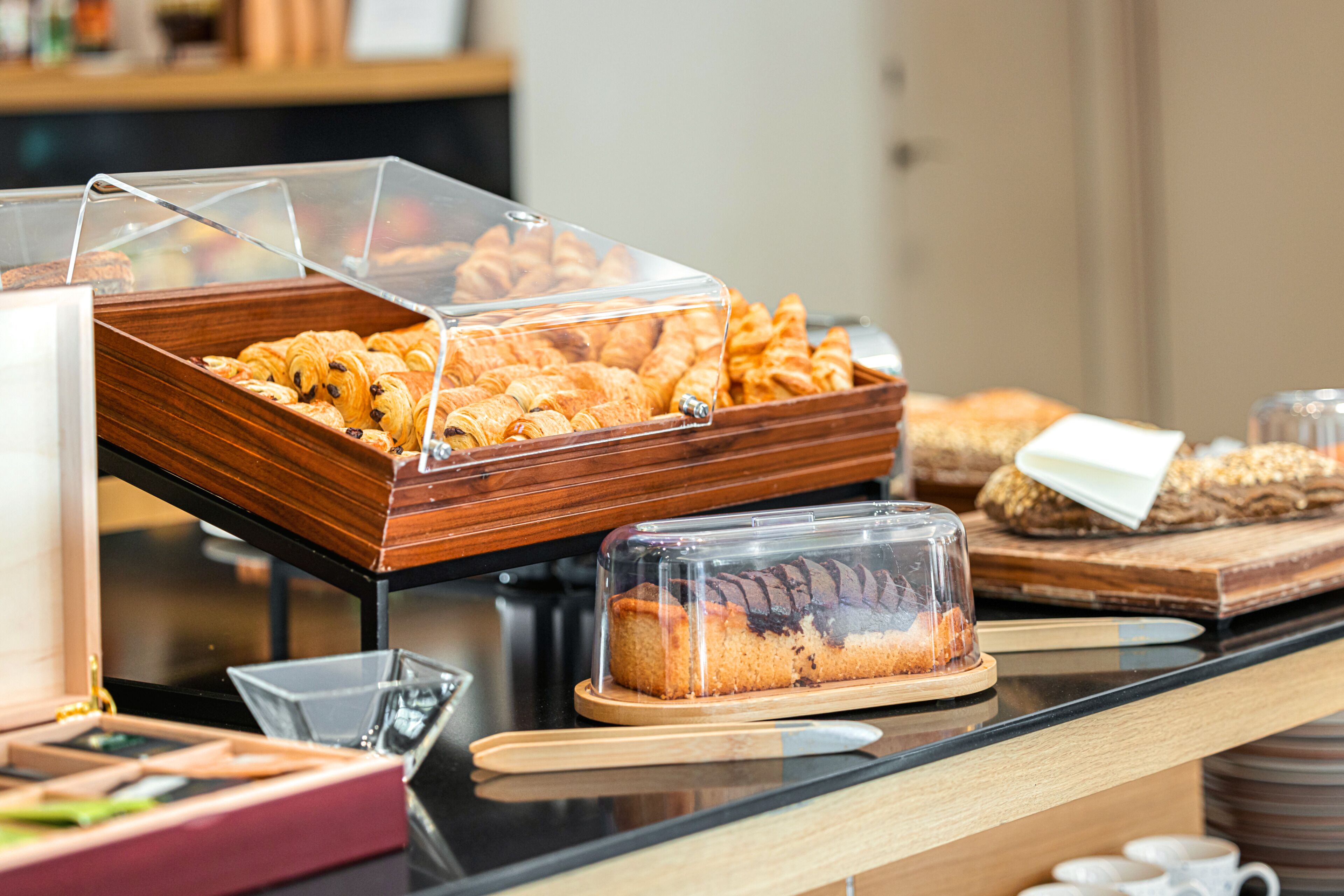 Mostrador de buffet con diversas opciones de panadería, incluyendo pasteles y pan, expuestos en recipientes transparentes.