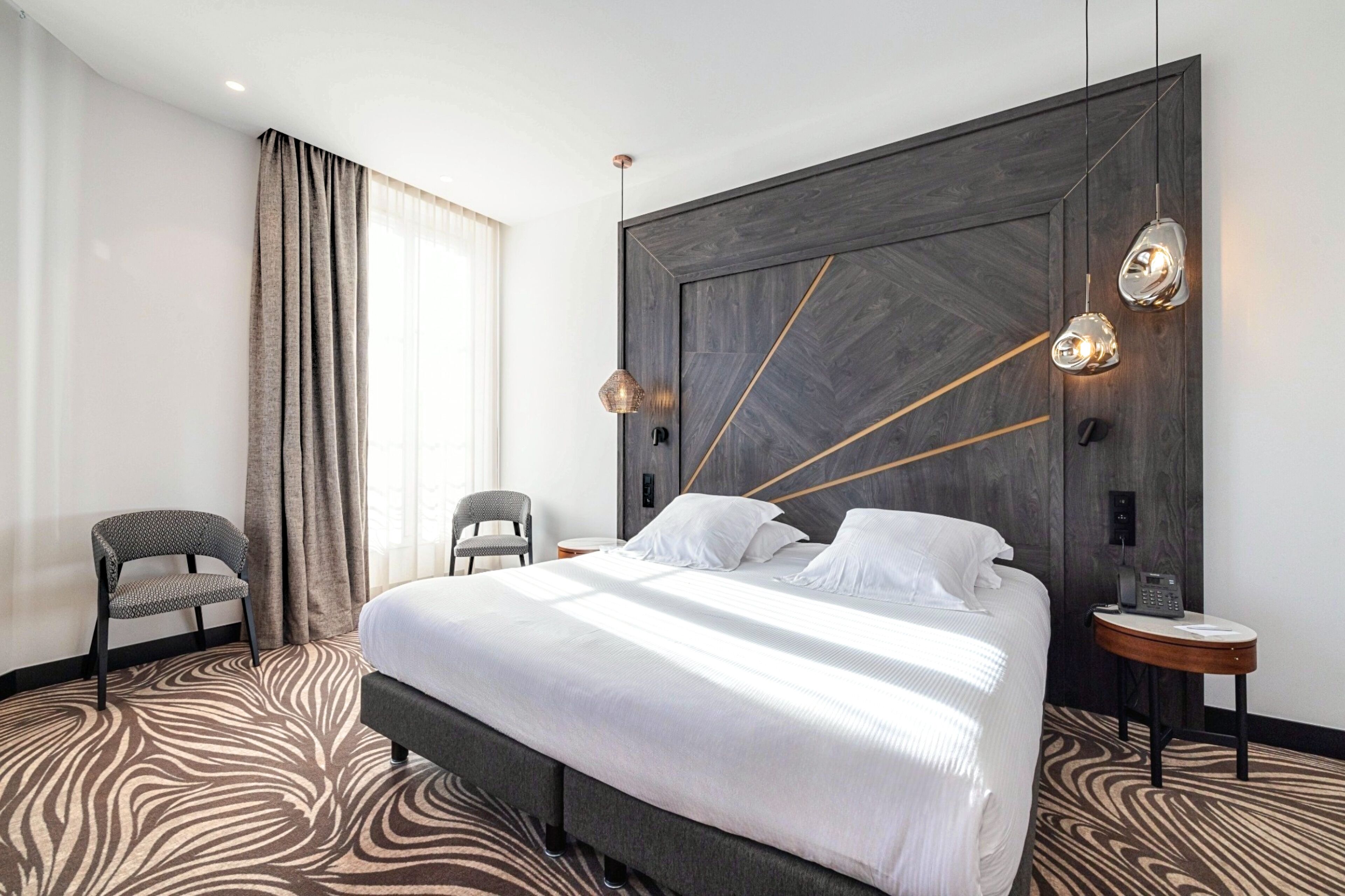 Ein modernes Hotelzimmer mit einem großen Bett, einem Holzkopfende, einem Zebra-Teppich, einem kleinen runden Tisch und einem Stuhl.