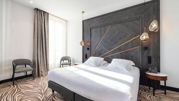 Ein modernes Hotelzimmer mit einem großen Bett, einem Holzkopfende, einem Zebra-Teppich, einem kleinen runden Tisch und einem Stuhl.