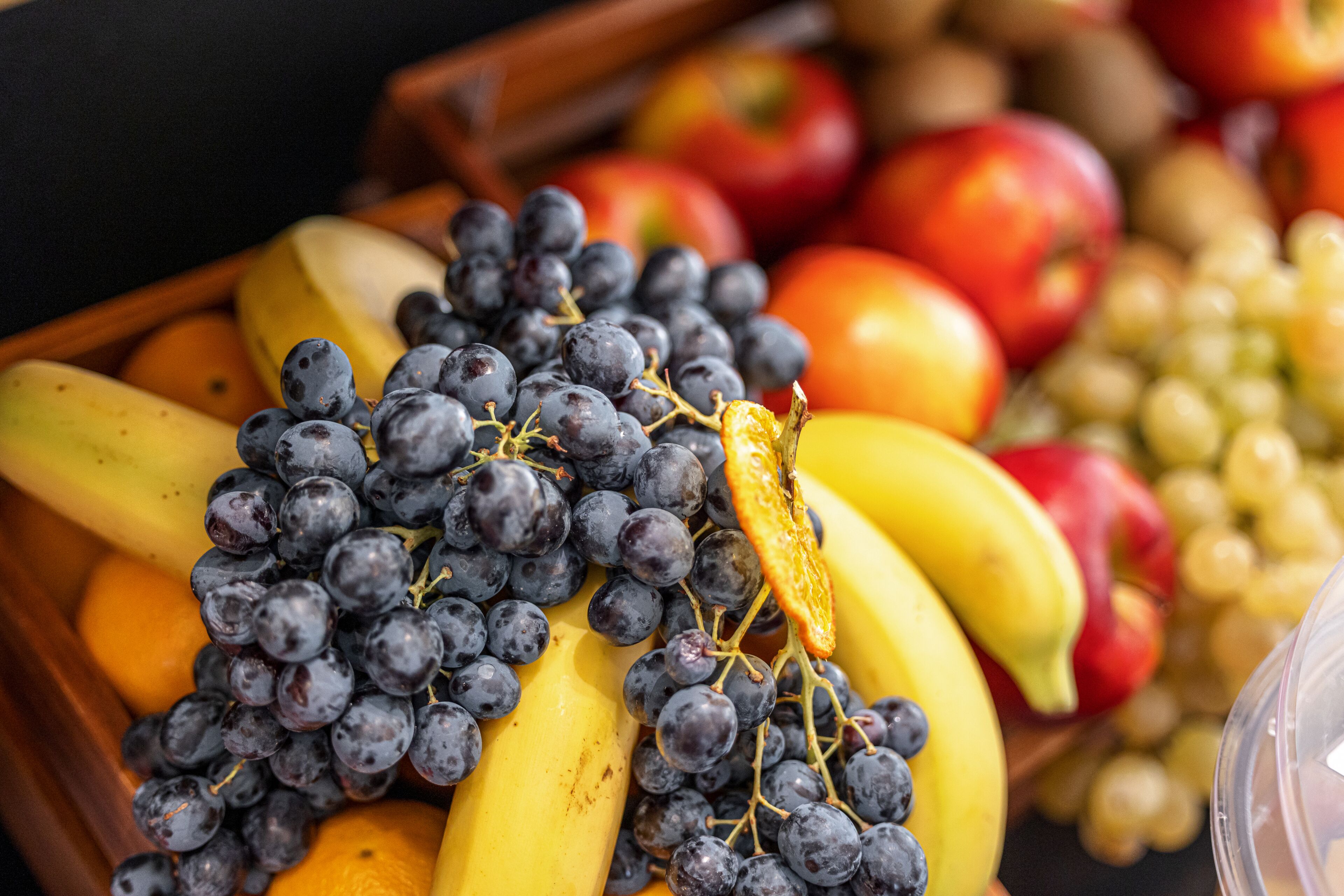 Una cesta de mimbre con plátanos, uvas y manzanas.