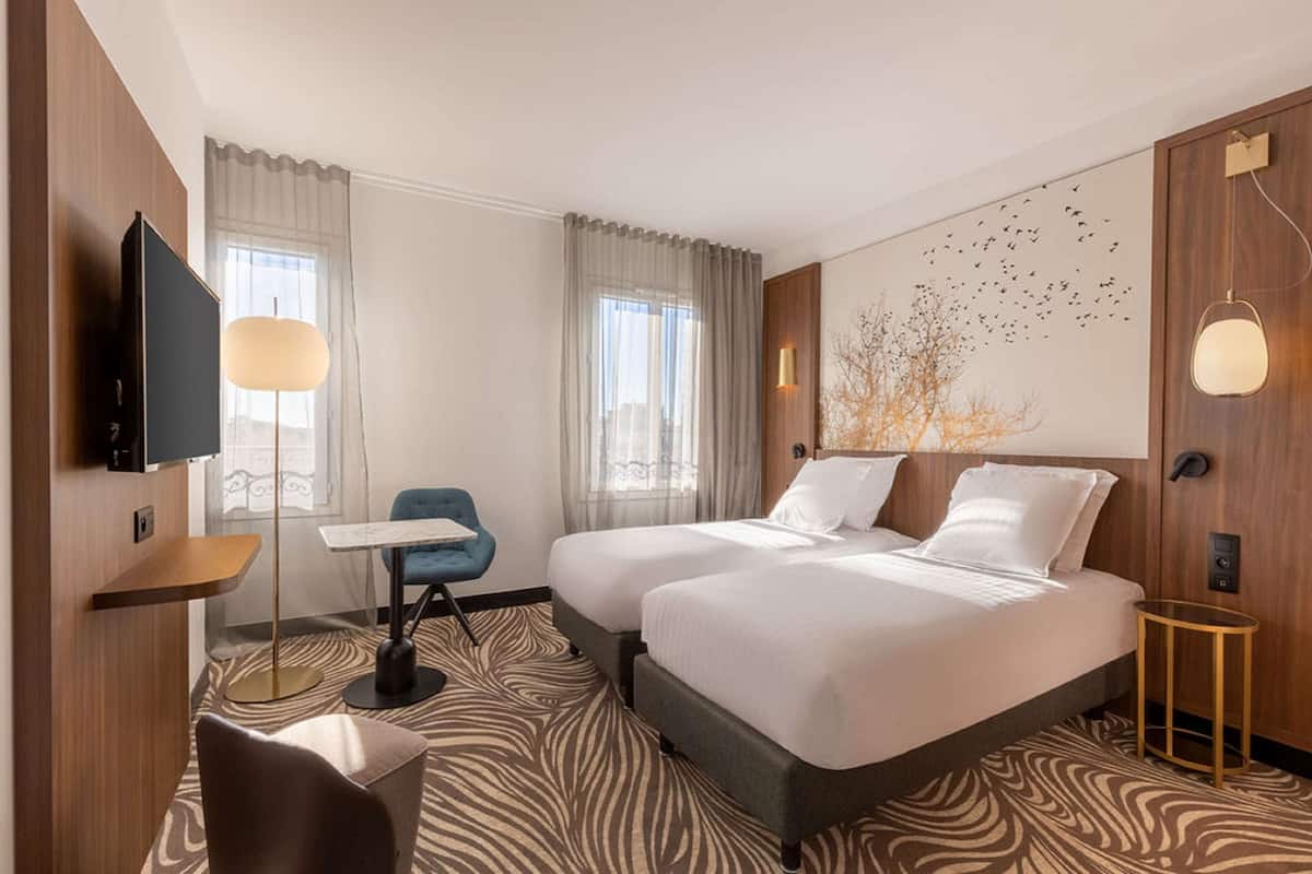 A hotel room with two beds, a flat-screen TV, a desk, a chair, and a large window with curtains.