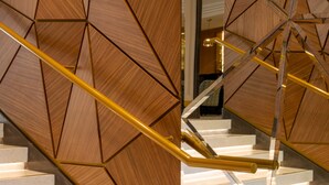 Una escalera moderna con paneles de madera geométrica y barandilla dorada.