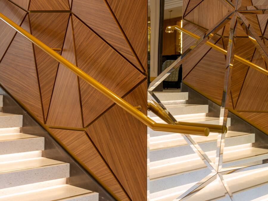 A modern staircase with geometric wooden panels and a golden handrail.