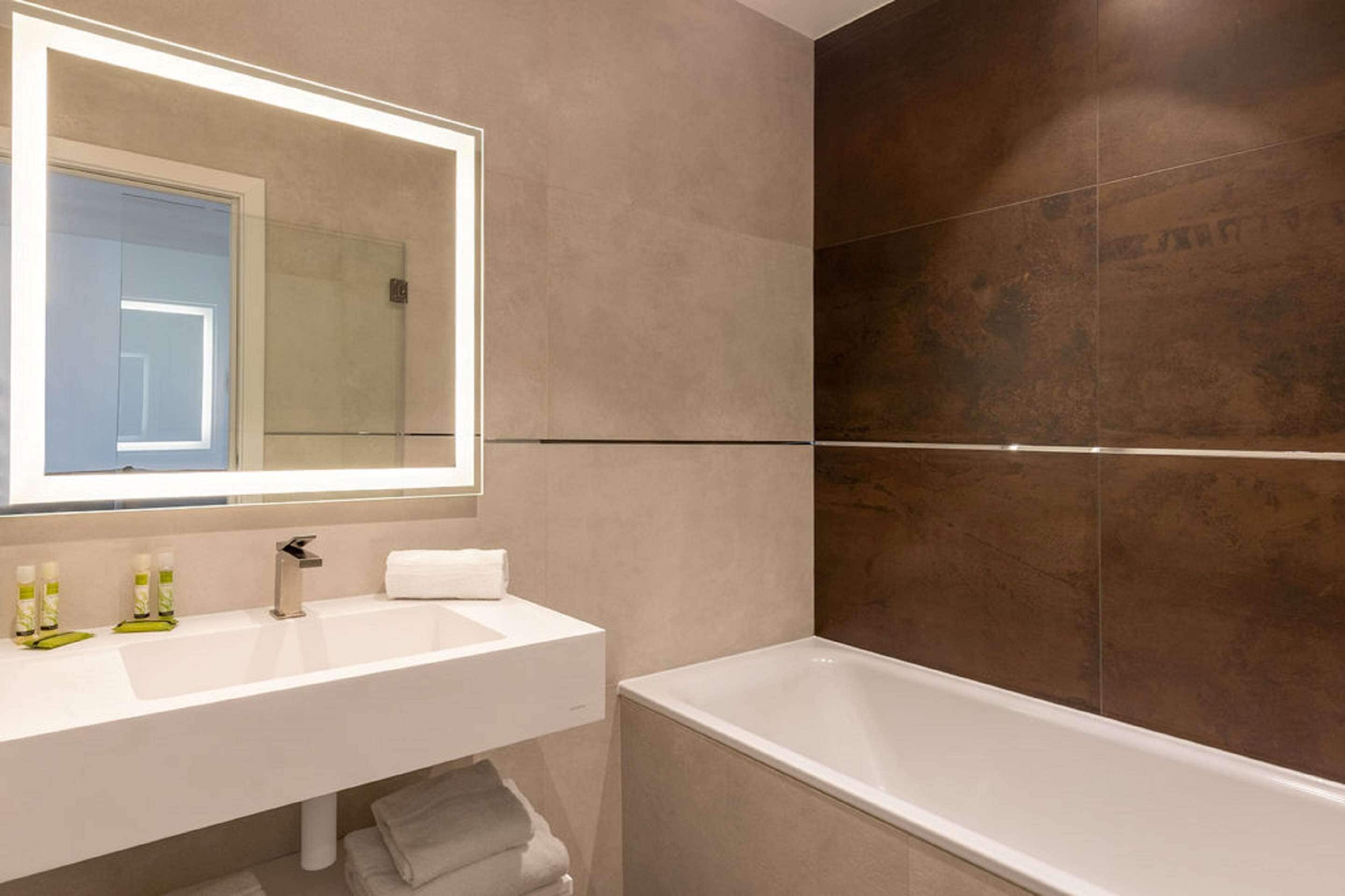A modern bathroom with a large mirror, white sink, and a bathtub.