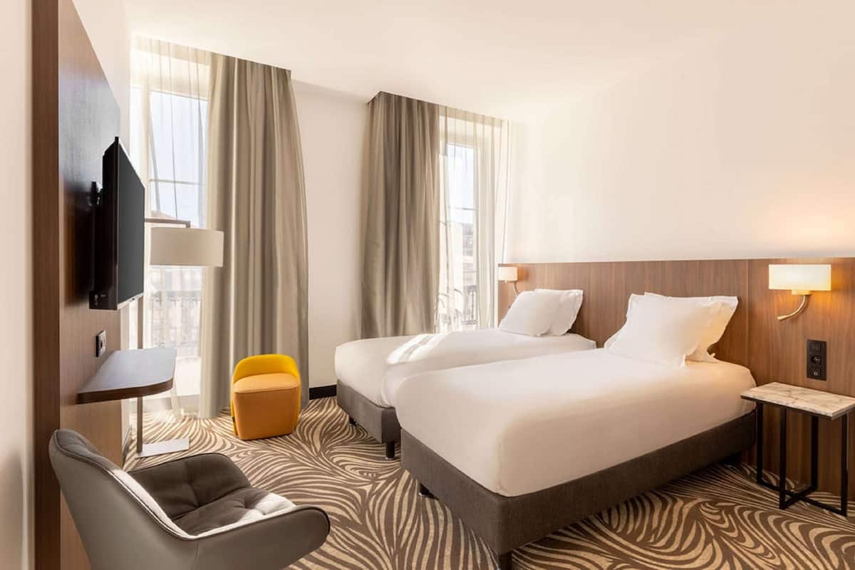A hotel room with two beds, a TV, a small table, a chair, and a sofa.