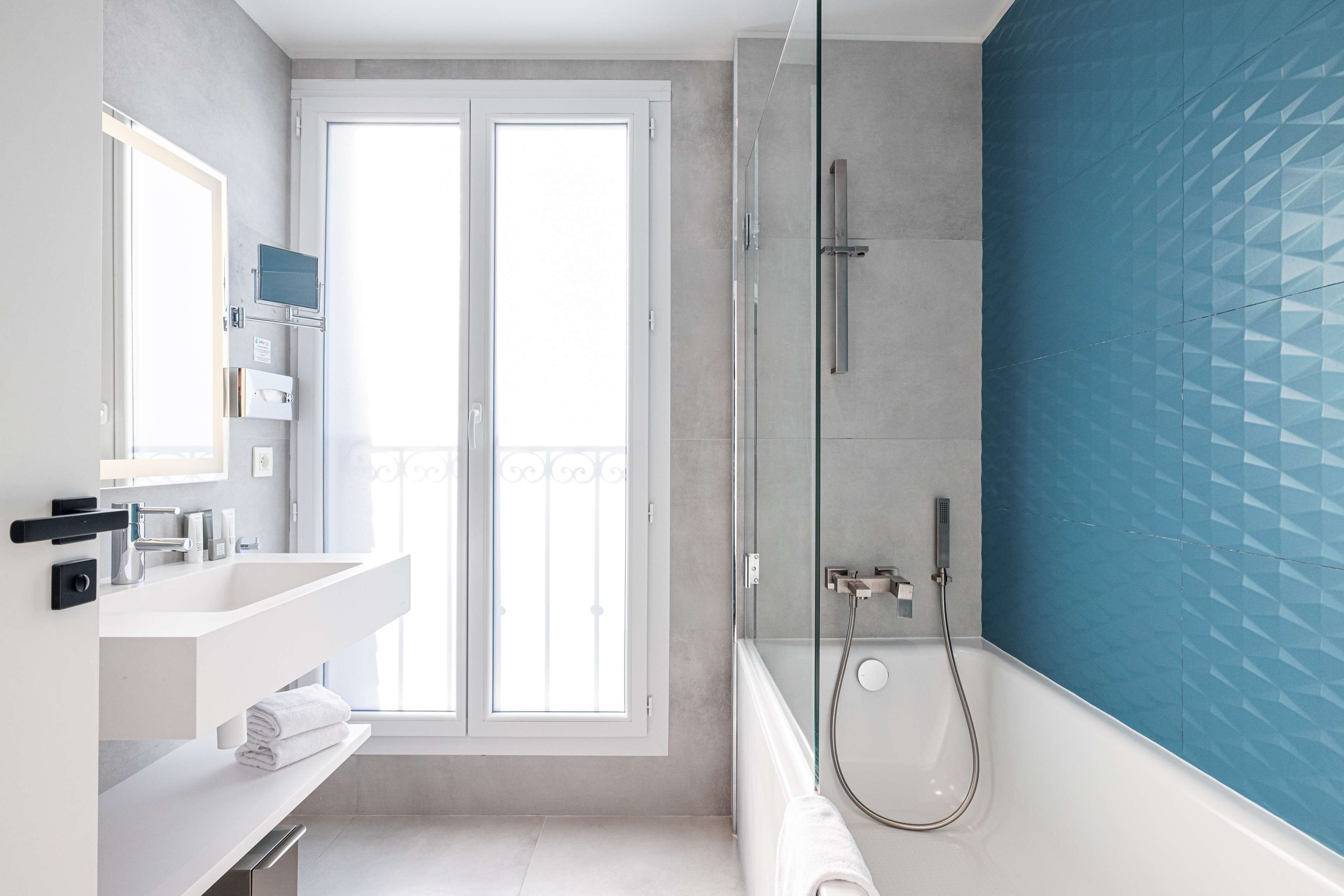 A modern bathroom with a large window, a glass-enclosed shower, and a white vanity.