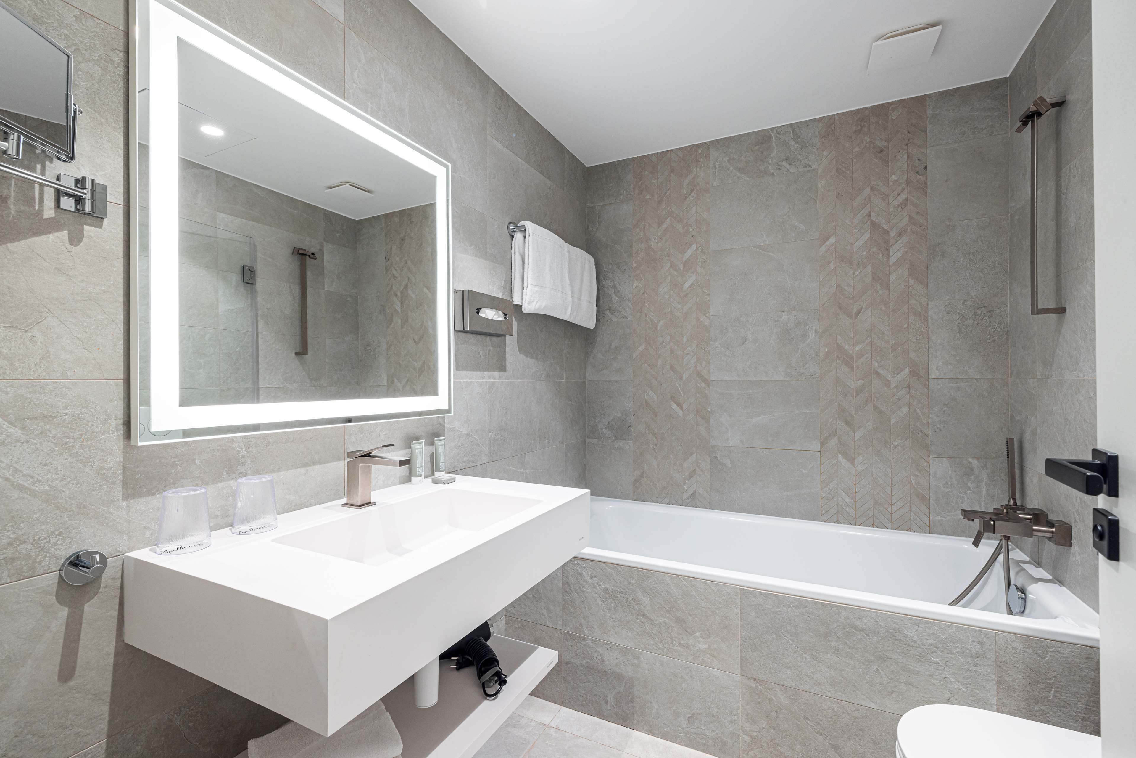 Un baño moderno con un espejo grande, dos lavamanos, una bañera y una ducha.
