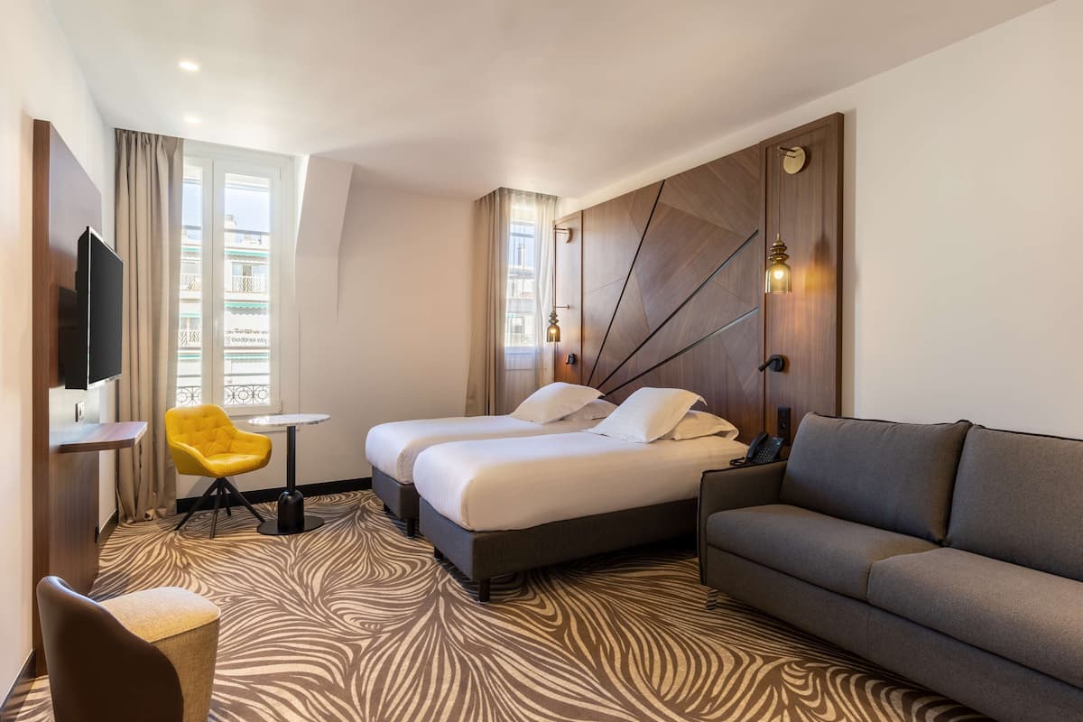 A hotel room with two beds, a sofa, a small table, a TV, and a window with curtains.