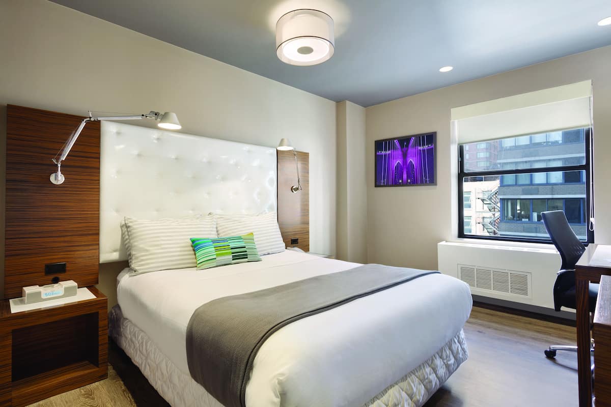 Quarto de hotel moderno com uma cama grande, uma escrivaninha e uma janela com vista para a cidade.