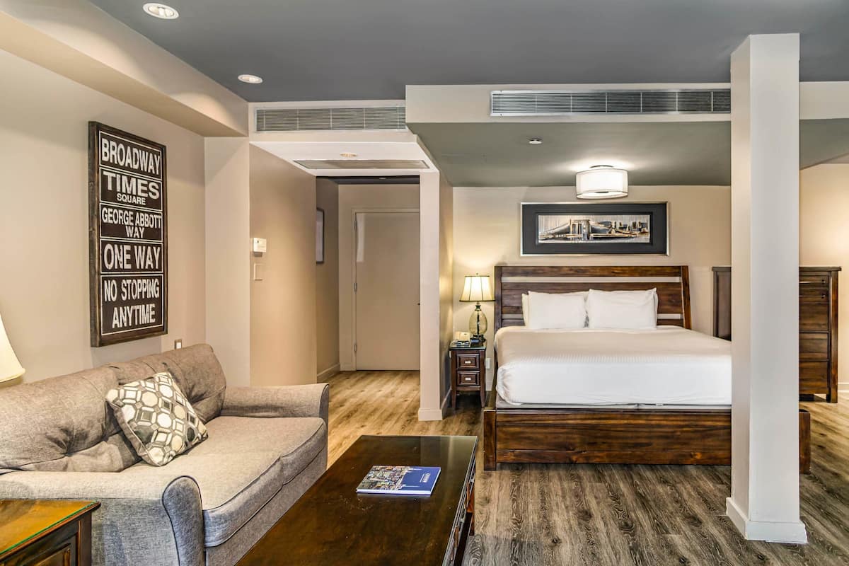 Quarto de hotel com uma cama, um sofá, uma mesa de centro, um abajur e um quadro na parede.
