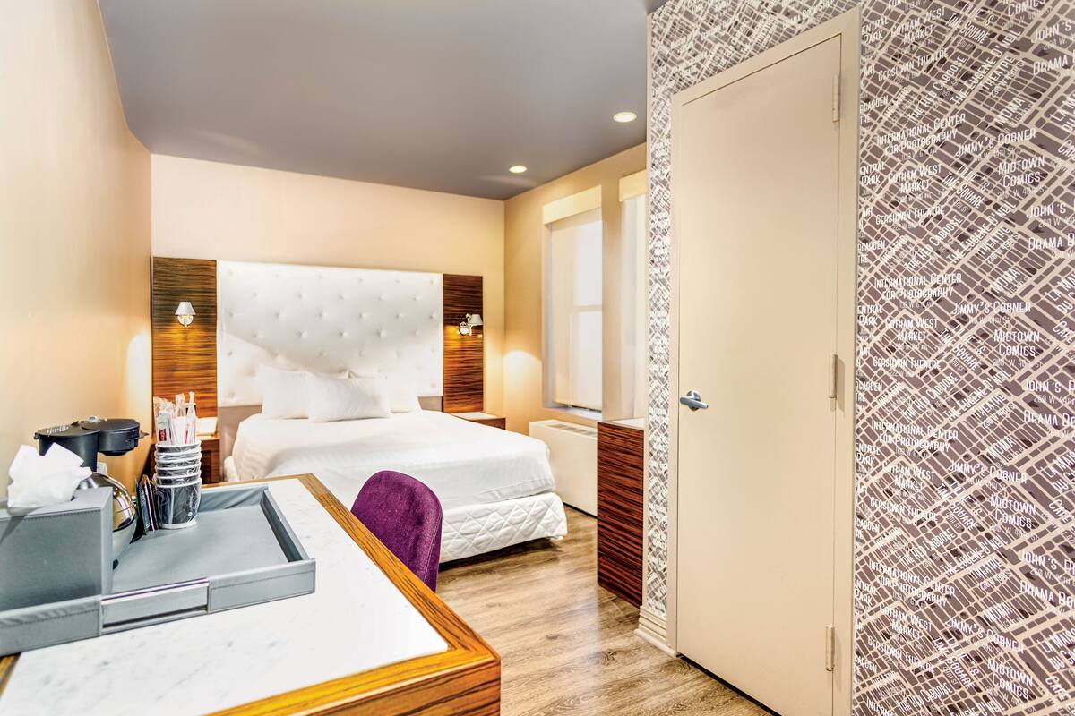 Quarto de hotel com uma cama grande, mesas de cabeceira, uma escrivaninha com cadeira e um guarda-roupa.