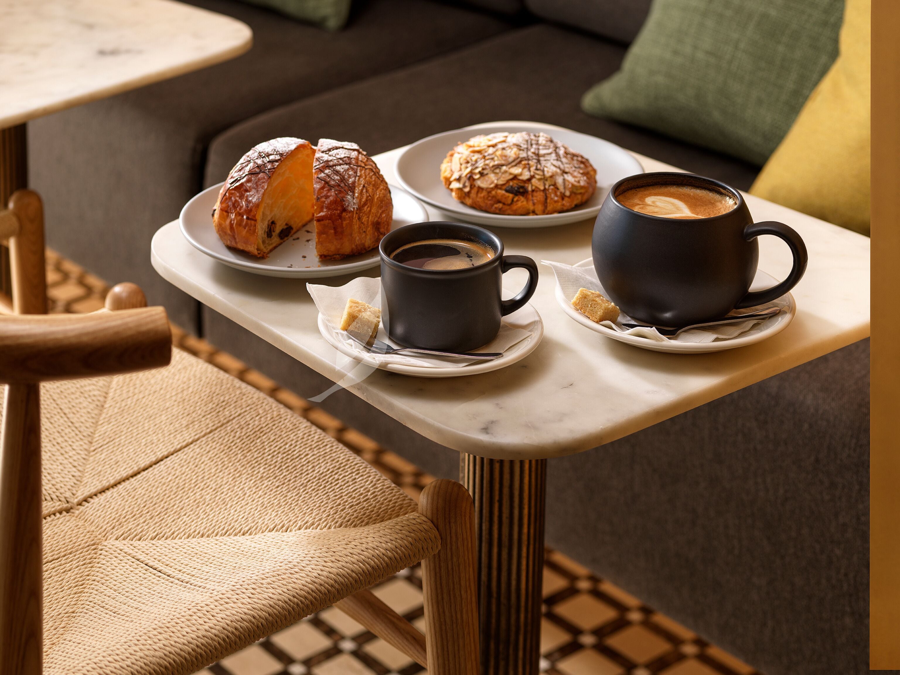 Uma bandeja com um croissant, um muffin e duas xícaras de café sobre uma mesa.