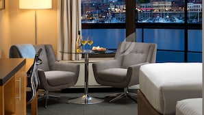 A hotel room with a city view, two armchairs, a small table with a bottle and glasses, and a bed. - Inn at Laurel Point  (Victoria)
