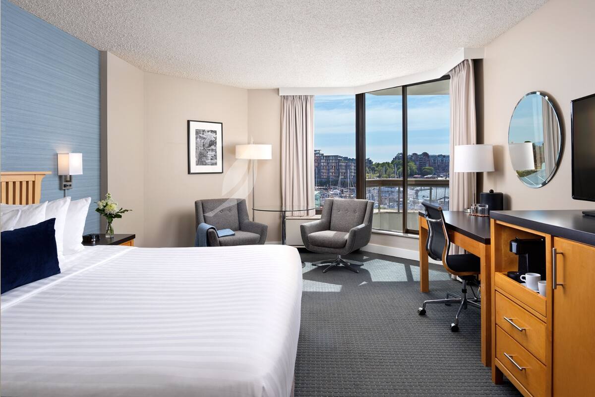 Habitación de hotel con una cama grande, un escritorio, una silla, un televisor y vistas de la ciudad.