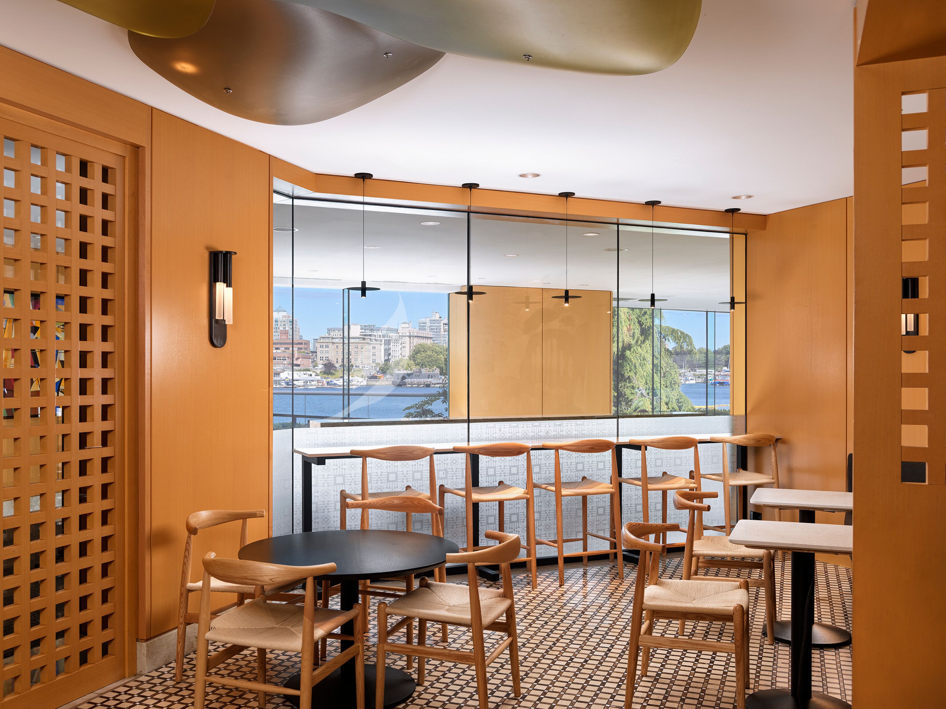 A modern interior with a view of a cityscape through large windows, wooden furniture, and a patterned floor.