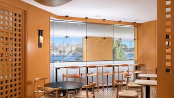 A modern interior with a view of a cityscape through large windows, wooden furniture, and a patterned floor.