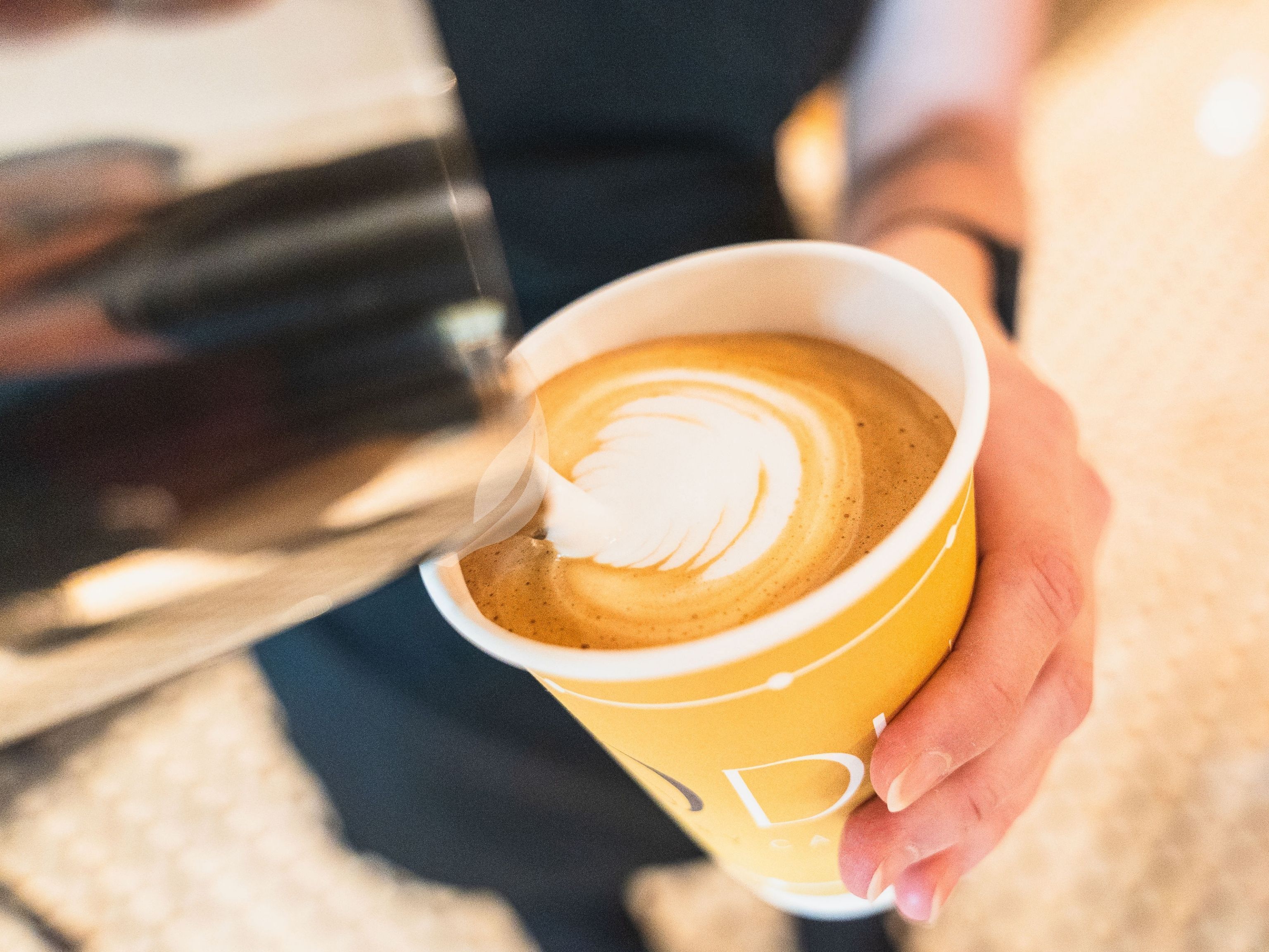 Uma pessoa segurando uma xícara de café com arte de latte.