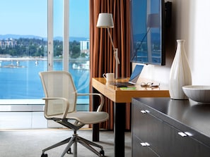 A modern hotel room with a desk, chair, laptop, lamp, and a large window offering a view of a body of water and distant buildings. - Inn at Laurel Point  (Victoria)