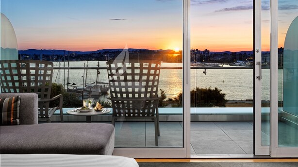 A balcony with a view of a sunset over a body of water, featuring a dining table and chairs.