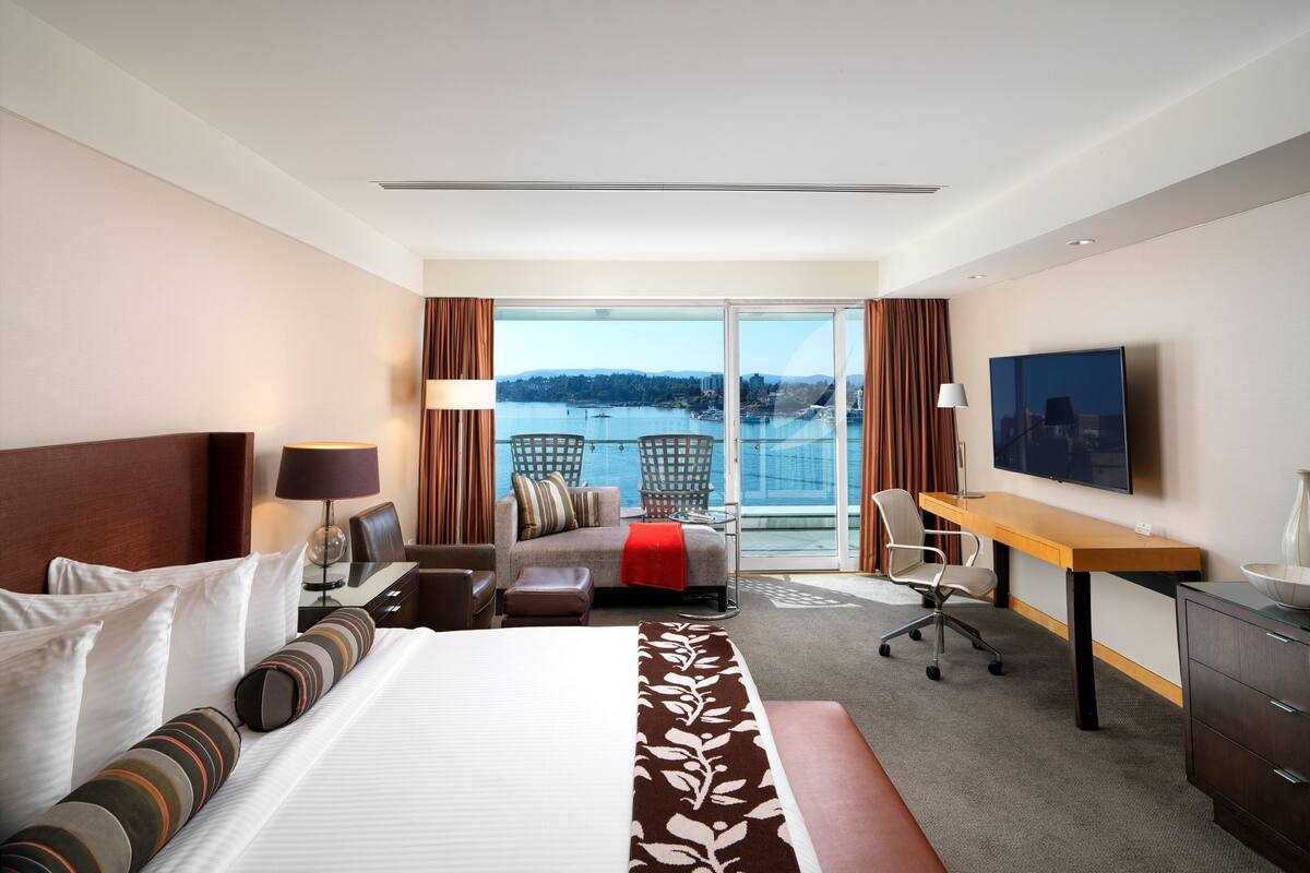 Habitación de hotel con una cama grande, un escritorio, una silla, un televisor y vistas a una masa de agua.