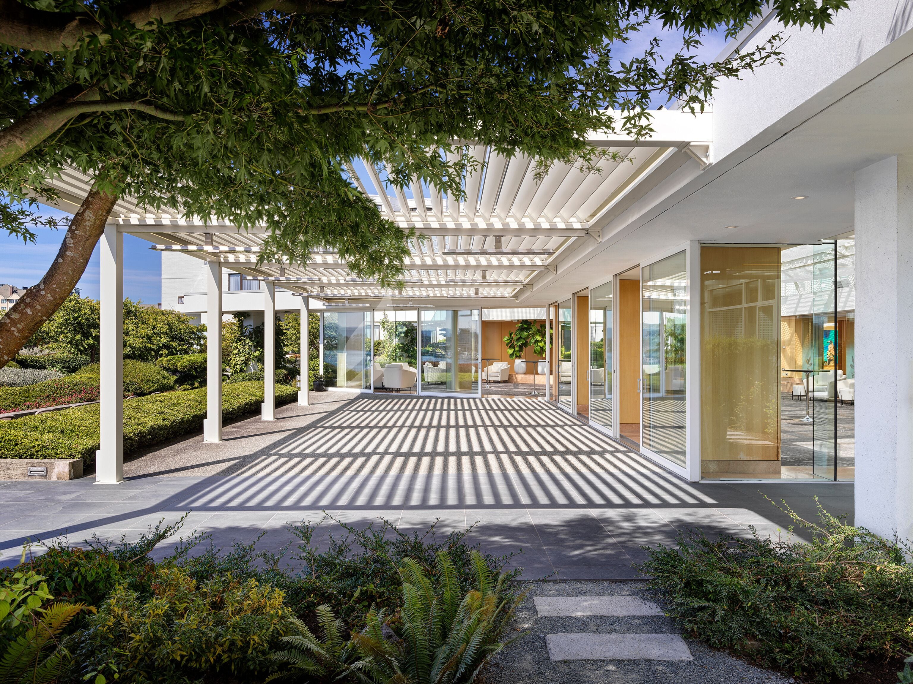 Un patio moderno all'aperto con pavimento decorato, porte in vetro e una struttura in pergola bianca.