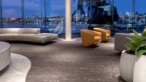 A modern lounge with a curved sofa, two armchairs, and a round coffee table. A large window offers a city view at dusk.