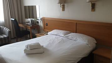 A hotel room with a large bed, a desk with a telephone, a chair, and a lamp.