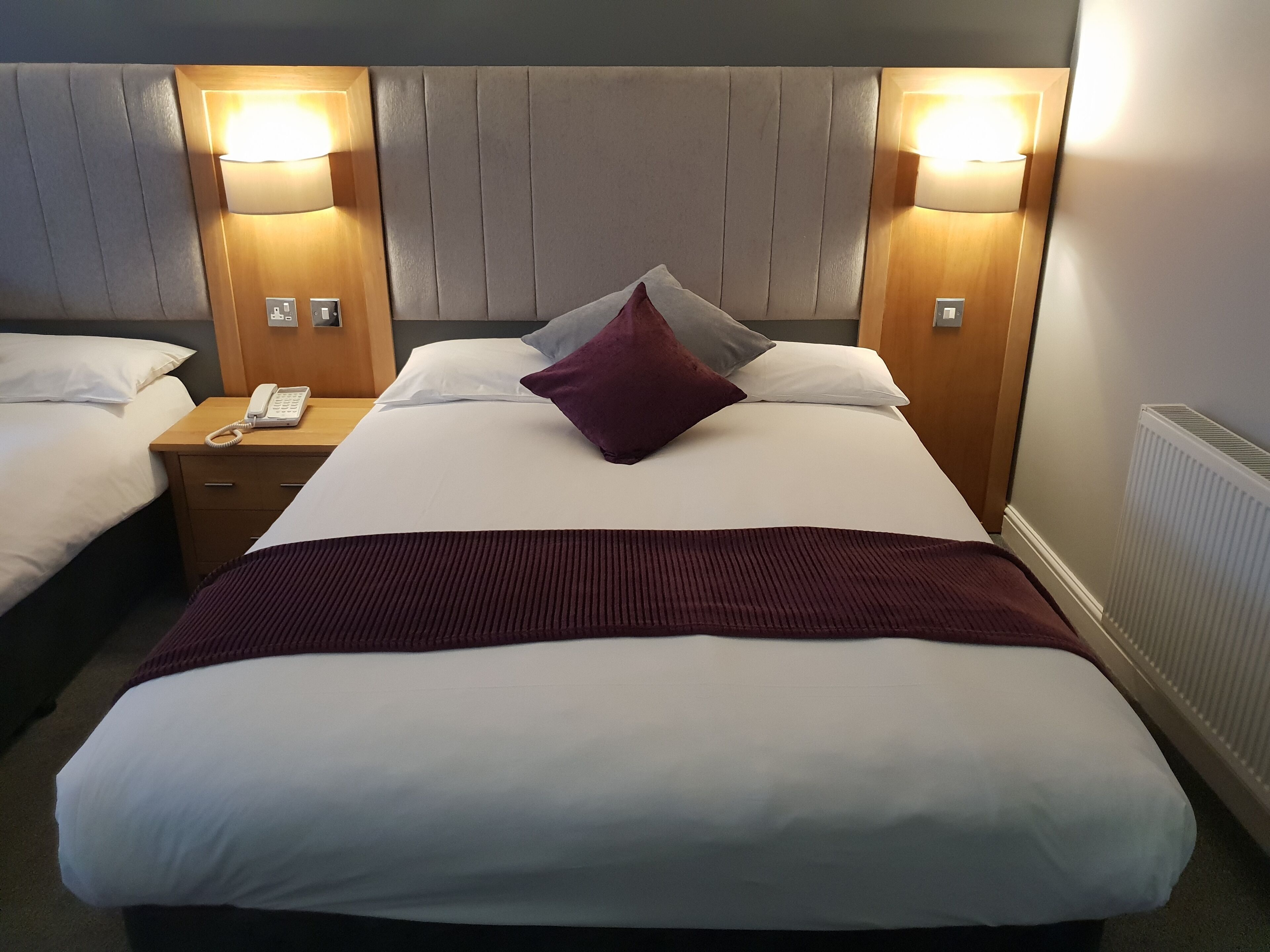 A hotel room with a large bed, two bedside tables, a telephone, and two wall-mounted lamps.