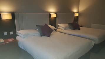 Habitación de hotel con dos camas individuales, cada una con sábanas blancas y una almohada. Hay lámparas de pared a cada lado de las camas.