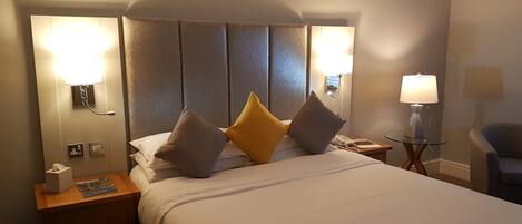 Et hotelværelse med en stor seng, to sengeborde med lamper, en stol og et vægmonteret telefonapparat.