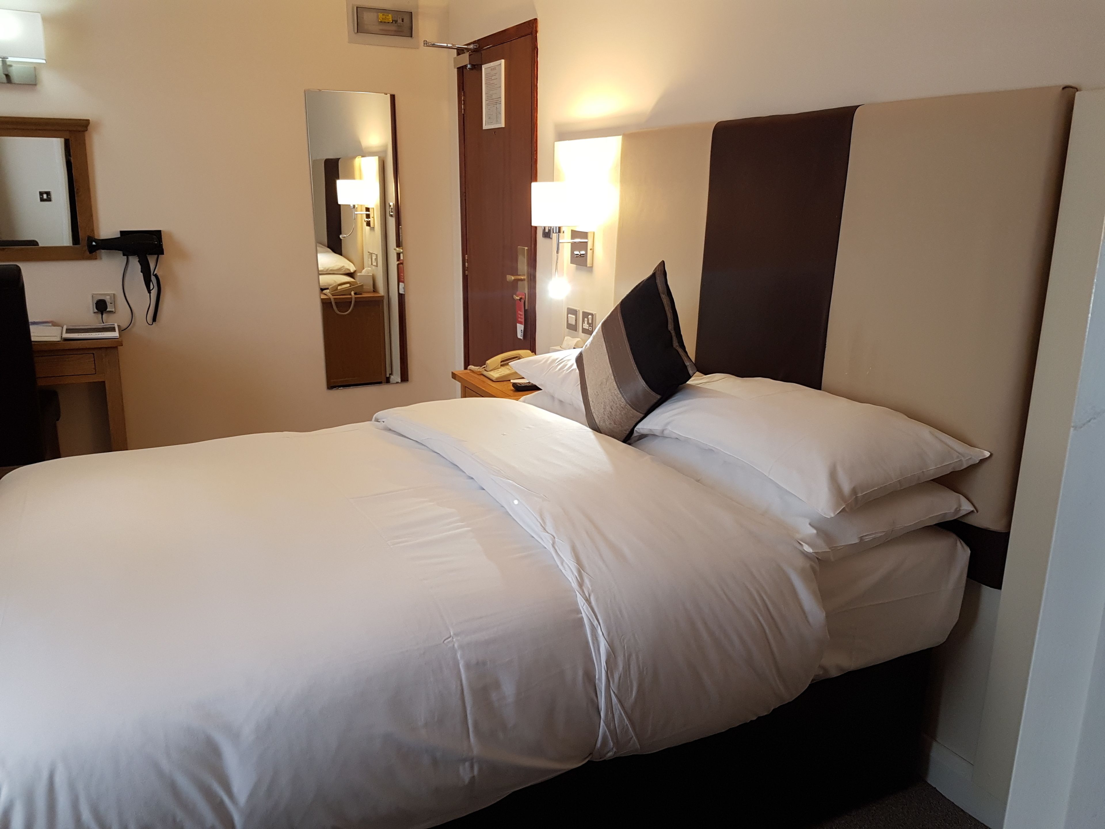 Habitación de hotel con una cama grande, un escritorio con teléfono, un espejo y una lámpara de pared.