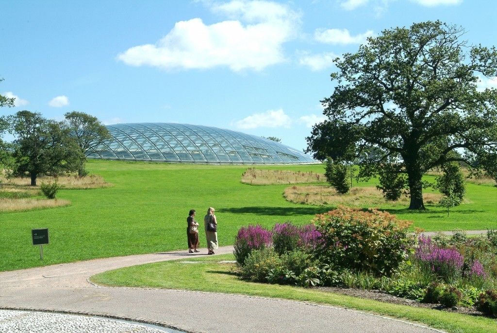 A large greenhouse structure in a landscaped area with a pathway leading to it.