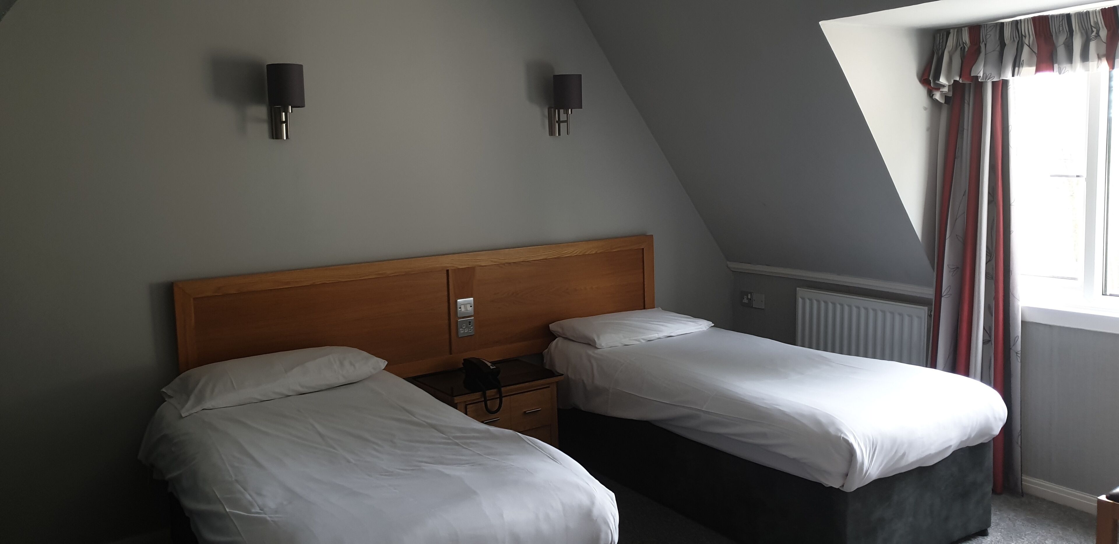 Une chambre avec deux lits, une tête de lit en bois, une table de chevet avec un téléphone et un radiateur.