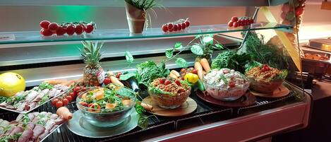A buffet with various food items including salads, fruits, and meats.