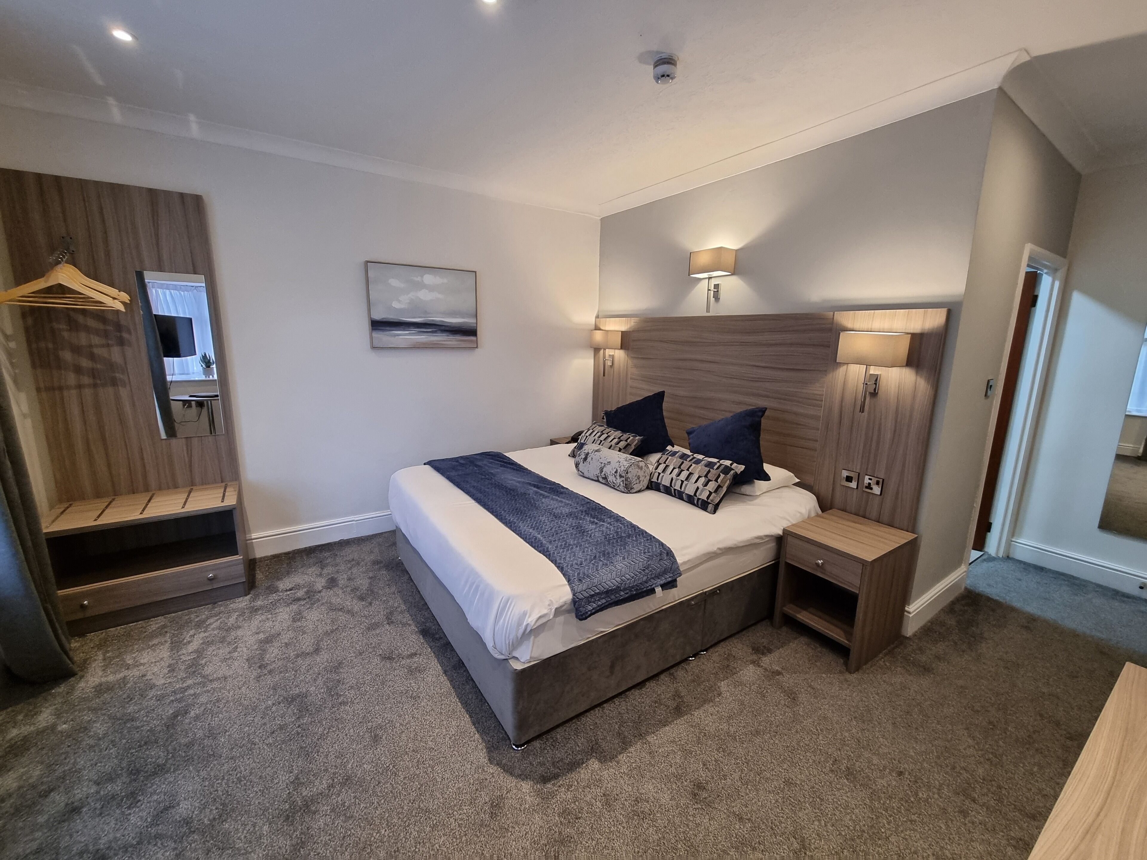 A modern bedroom with a large bed, bedside tables, a wardrobe, and a mirror.