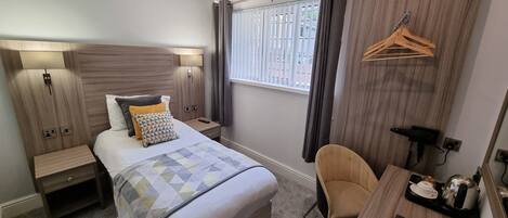 Ein modernes Hotelzimmer mit Bett, Nachttischen, einem Schreibtisch mit Stuhl, einem Fenster mit Vorhängen und einem Wandhänger.