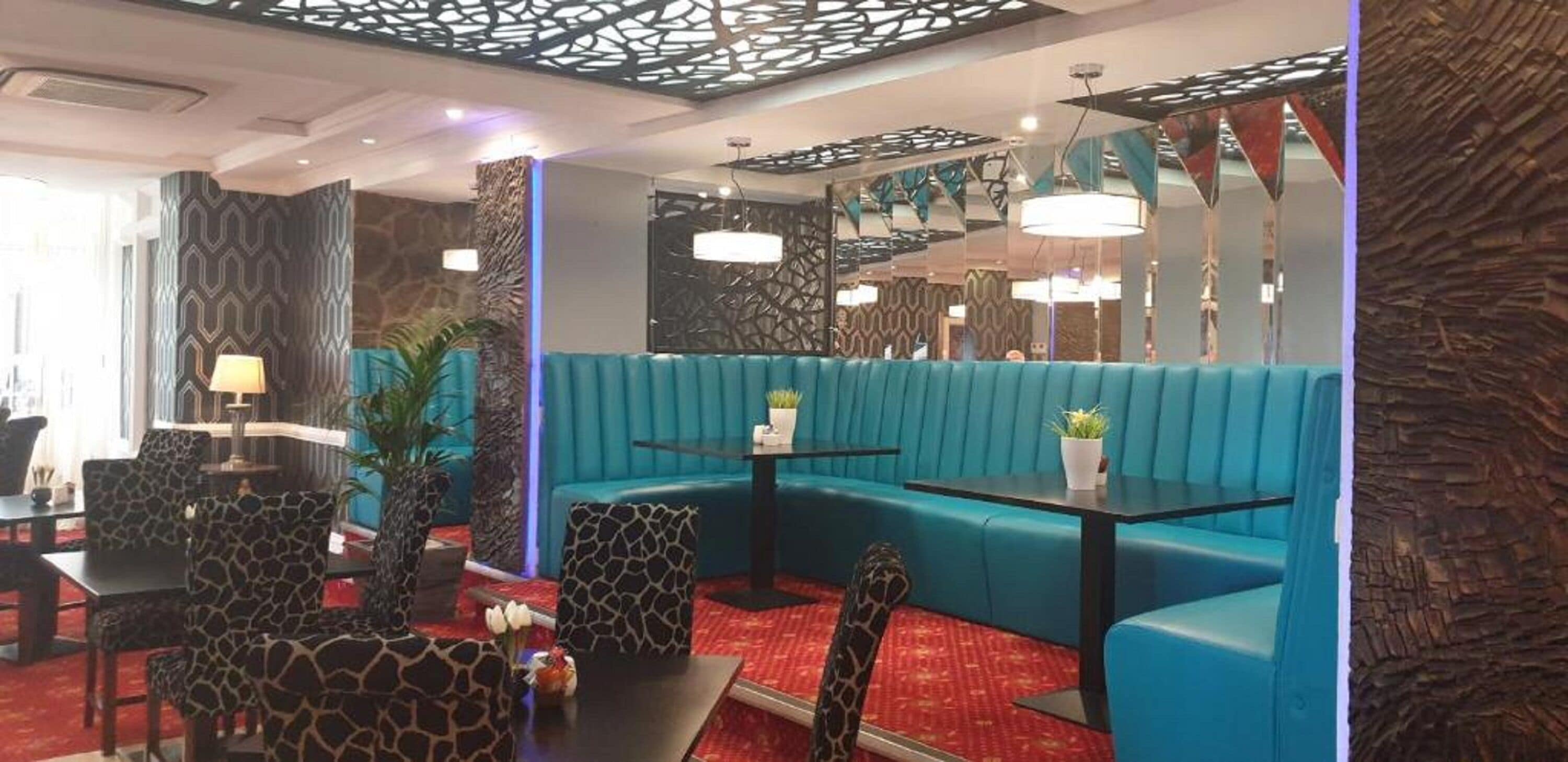 Un'area lounge moderna con sedute color petrolio, poltrone fantasia e tappeto rosso.
