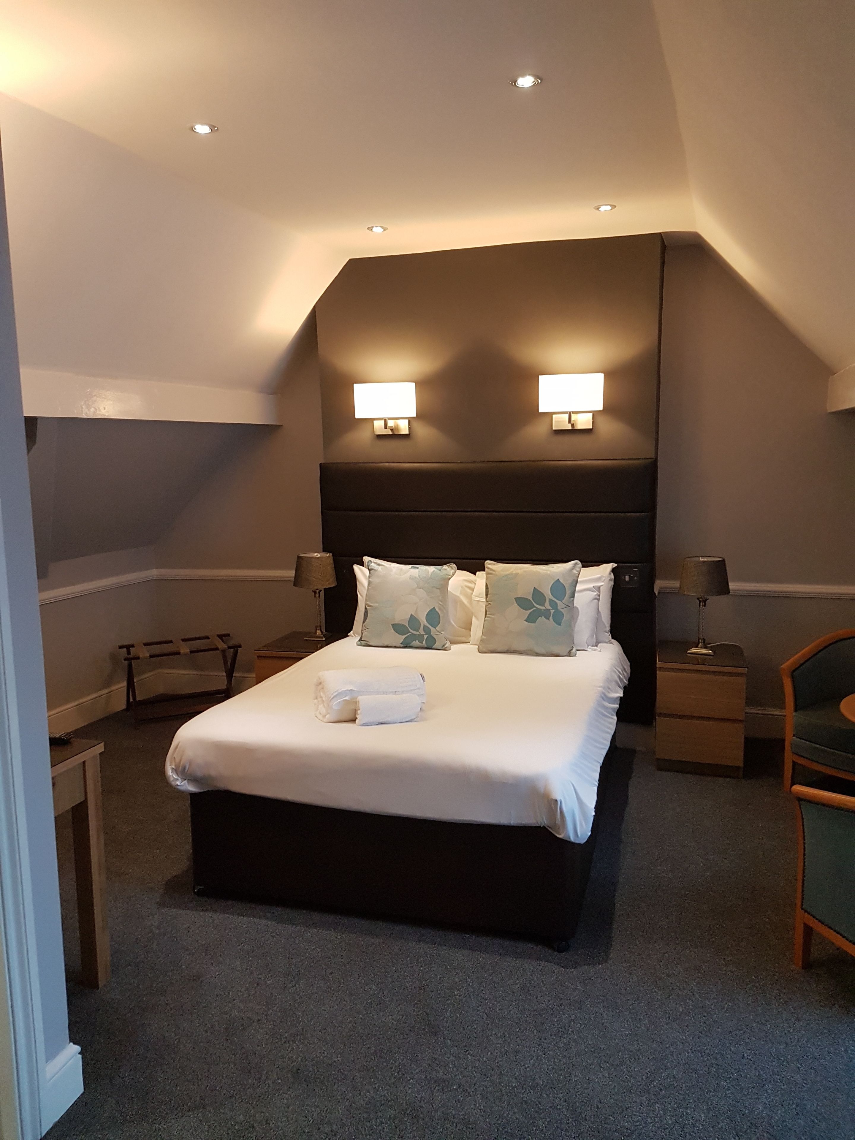 A hotel room with a large bed, two bedside lamps, a nightstand, a chair, and a small table.