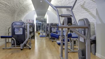 A gym with various exercise machines, a wooden floor, and white walls.