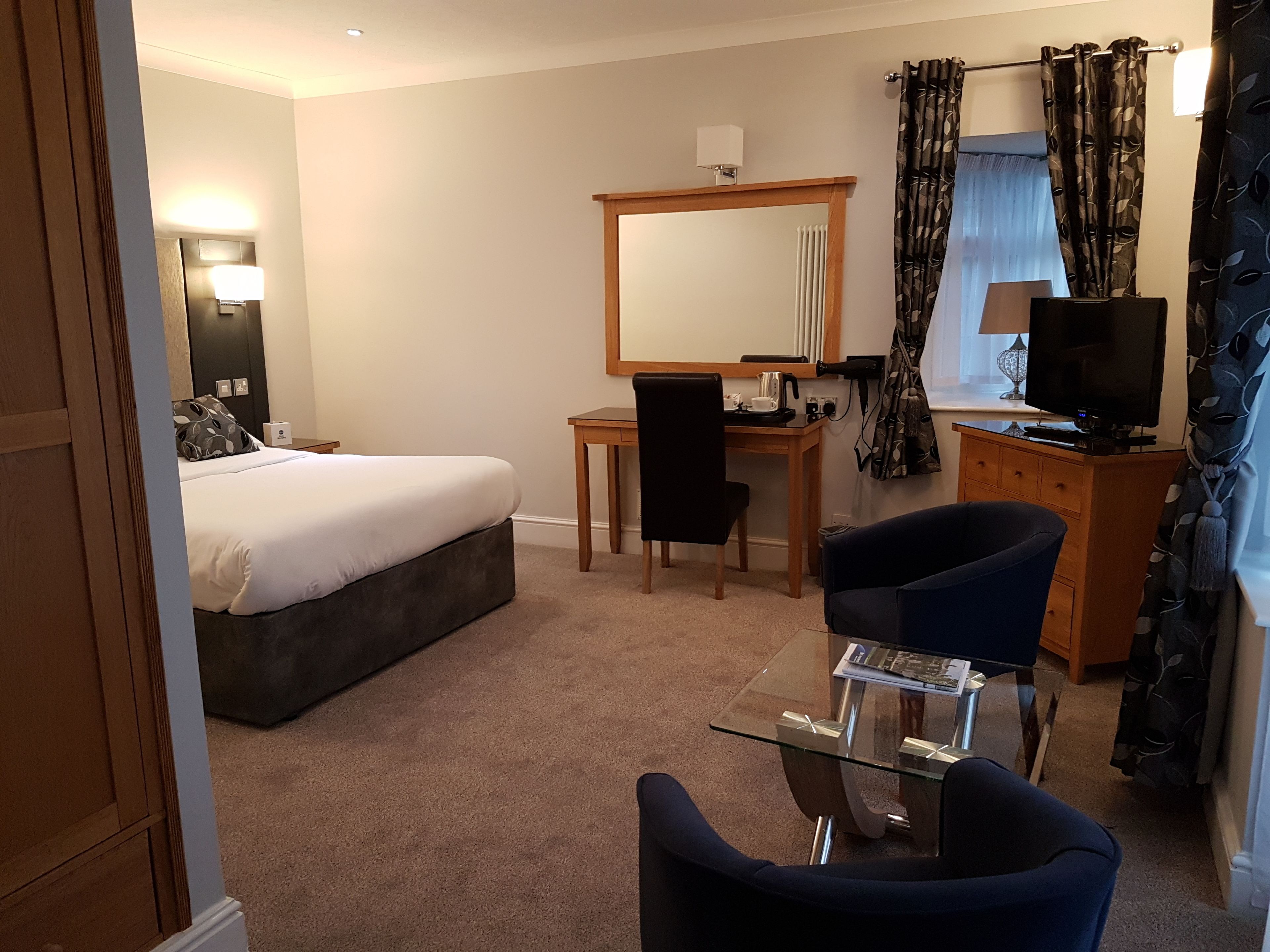 Une chambre d’hôtel avec un lit, un bureau, une chaise, une télévision et un miroir.