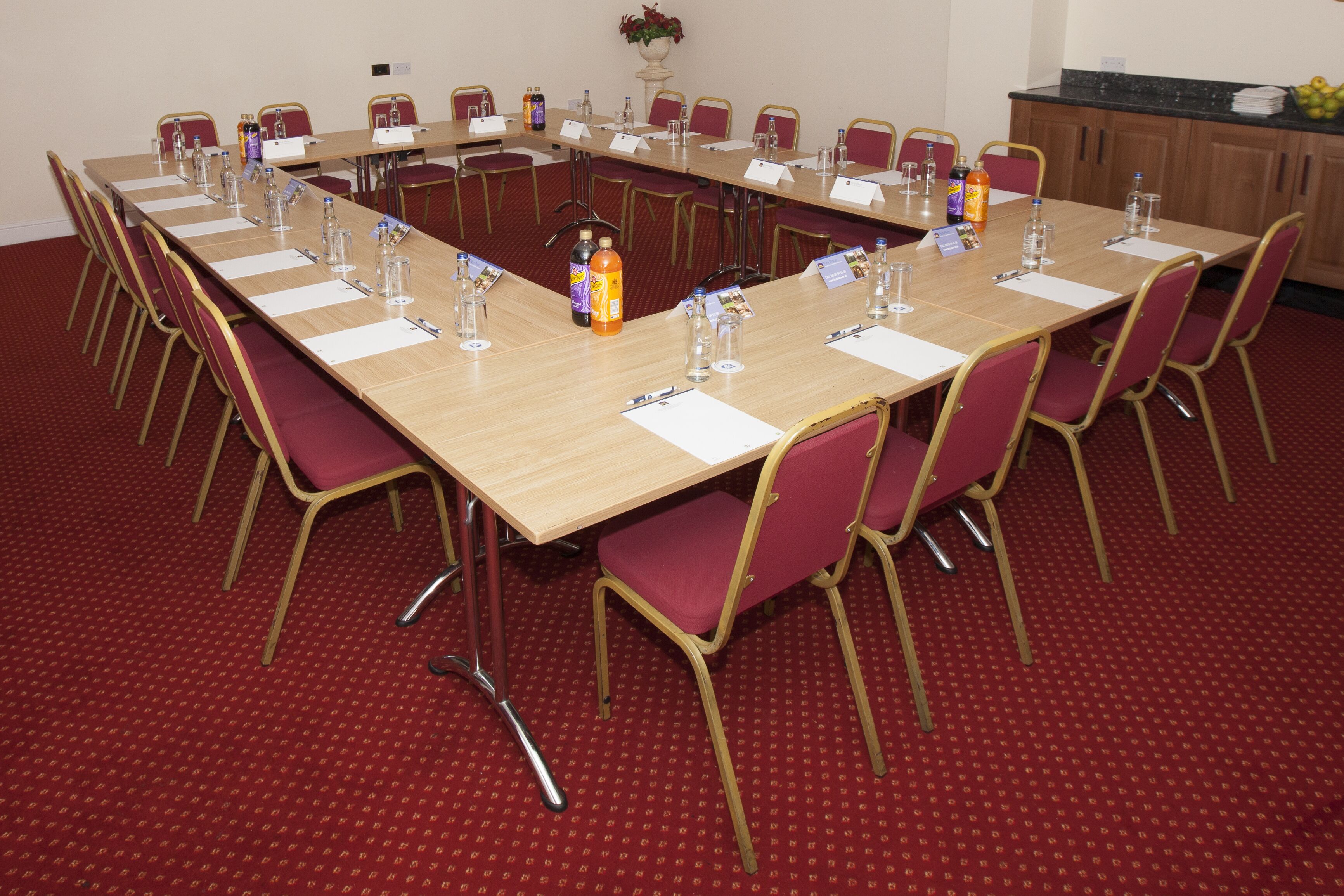 Un salón de conferencias con una larga mesa, alfombra roja y sillas.